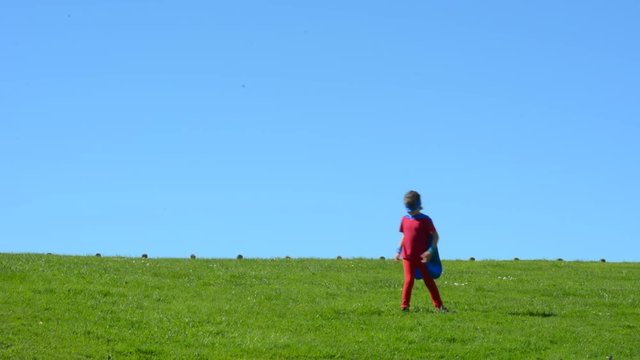 Superhero child (girl) runs in a green field against dramatic blue sky background with copy space. concept photo of Super hero, girl power, play pretend, childhood, imagination. Real people