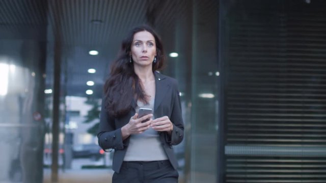 Business Woman Walking on Streets of Business District Holding Mobile Phone. Slow Motion. Shot on RED Cinema Camera in 4K (UHD).