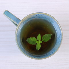 Lemon balm in cup of herbal drink on white wooden table