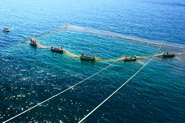 Old small fishing boats with fishermen drawing out nets in dark blue sea.