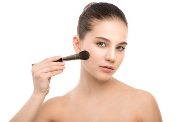 Fototapeta premium Portrait of beautiful young brunette woman with clean face. Beauty spa model girl with perfect fresh clean skin applying cosmetic brush. Youth and skin care concept. Isolated on a white background.