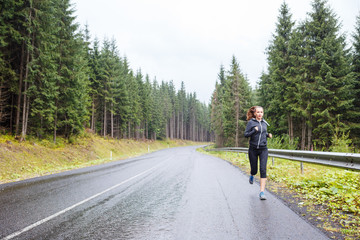 Obraz premium Young slim woman jogging on road at rainy morning