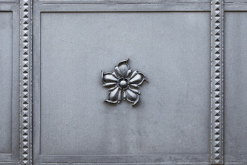 Geschmiedetes, graues Metalltor mit einem einzelnen Blumenornament in der Mitte.