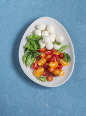 Fresh salad with tomatoes, mozzarella and basil. Caprese salad. On a blue background, top view