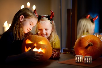 Two pretty young sisters in halloween costumes carving a pumpkin together