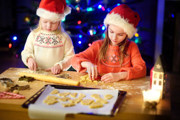 Two adorable little sisters baking Christmas cookies by a fireplace