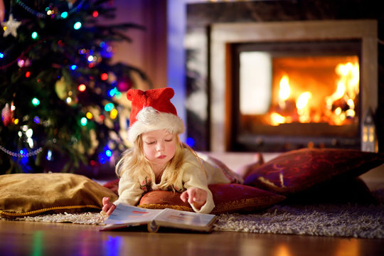 Adorable little girl reading a story book under a Christmas tree