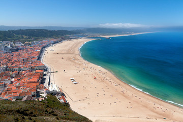 View over sandy beach coastline with ocean, sunlight, blue sky at Nazare, Portugal