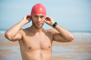 Portrait of a strong triathlon sportsman adjusting cap motivated for his open water summing workout routine on a beach.