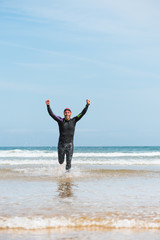 Fit sporty open water swimmer man running off shore on a beach rising arms up in victory sign after swimming triathlon competition exercise routine workout.