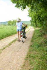 Naklejka premium Relaxing outdoor. Young woman riding bike through a field. Rear view.