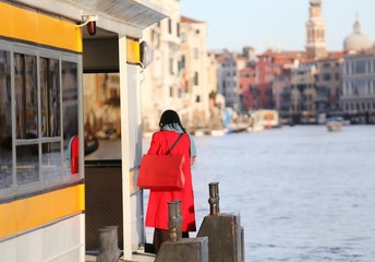 elegant woman dressed in red awaits vaporetto on the Grand Canal - obrazy, fototapety, plakaty