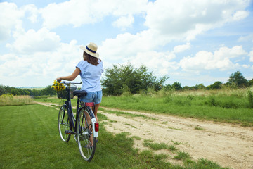 Obraz premium Relaxing outdoor. Young woman riding bike through a field. Rear view.