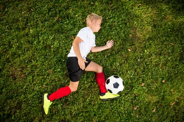 Foto op Canvas Aspiring young kid is seen training soccer / football on a local football field. Concept photo of a young football players seen from a birds perspective. © urbans78