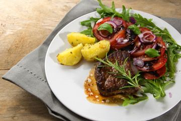 roasted beef filet mignon with potatoes and tomato arugula salad on a rustic wooden table