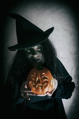 Witch holding halloween pumpkin. Low key. Computer added dirt, scratches, grain and vignette.