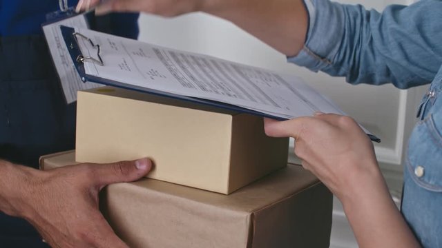 Closeup of hands of delivery man giving packages to female customer after she signing documents 