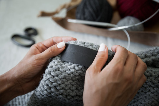 Woman sewing the genuine leather lable to the knitted clothing