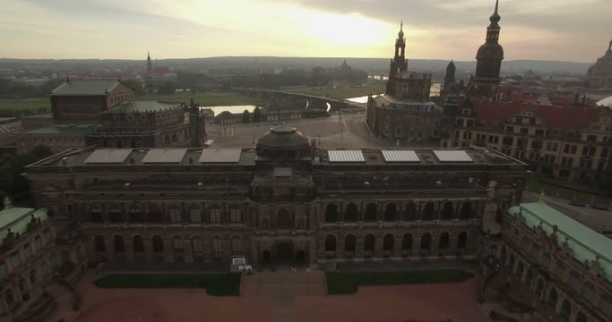Aerial camera flies backwards away from the Dresden skyline and over the Zwinger Palace. Shot on a cloudy morning at dawn