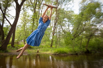Young beautiful woman in blue dress flying on the bungee above lake in a summer park.