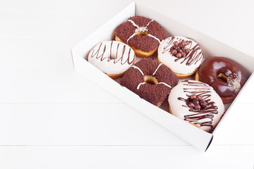 Colorful delicious donuts with sprinkles in a box on a white wooden background. Space for text