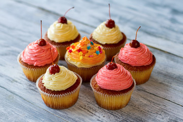 Colorful cupcakes with cherries. Small desserts on wooden surface. Soft dough and frosting. Tasty sweet treats.