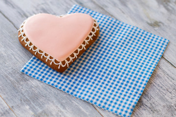 Obraz premium Heart-shaped biscuit on napkin. Pastry with light pink frosting. Sweet symbol of love. Live in joy.