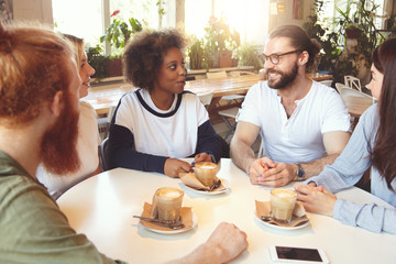Group of friends of diverse ethnicities relaxing at coffee shop, drinking cappuccino, talking to each other, looking happy and carefree. University mates sitting at canteen discussing future plans