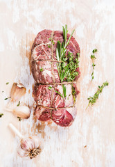 Raw uncooked roastbeef meat cut with rosemary, thyme and garlic on old white painted wooden background, top view, selective focus