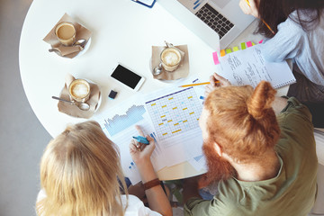 Cooperation and teamwork. Overhead shot of young businesspeople discussing plans, analyzing financial growth statistics of their small company, making notes on paper, studying charts and graphics