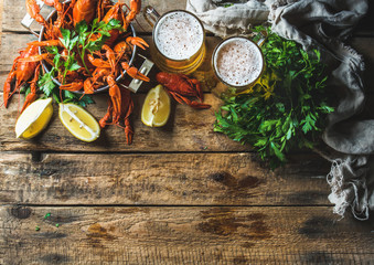 Fototapeta na wymiar Two pints of wheat beer and boiled crayfish with lemon and parsley over old wooden rustic background, top view, copy space