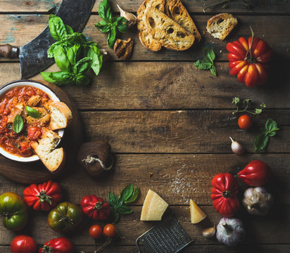 Homemade Italian roasted tomato and garlic soup in bowl with basil and Parmesan cheese over old rustic wood background with copy space in center, top view, horizontal composition