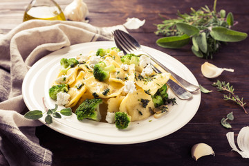 Italian ravioli with goat cheese, broccoli and herbs on old wooden background. Healthy food. Retro style toned