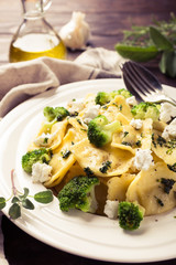 Italian ravioli with goat cheese, broccoli and herbs on old wooden background. Healthy food. Retro style toned