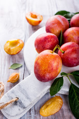Fresh plums on marble cutting board on old white wooden background. Selective focus. Healthy food concept. Copy space.