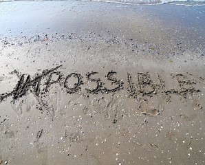 IMPOSSIBLE written with the letters IM deleted in the wet sand o