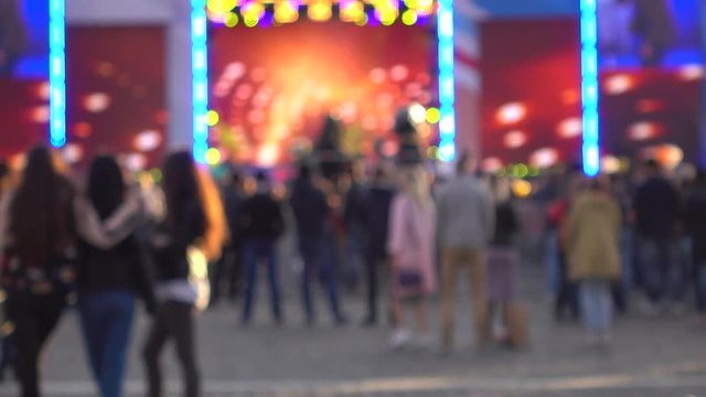Blurred people dancing at live show against outdoor stage. 4K background bokeh shot