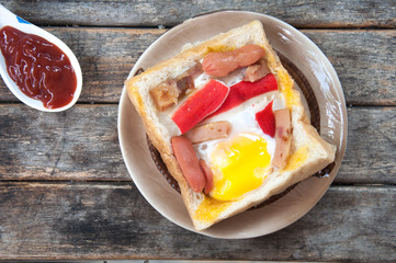 Egg, hotdog and crab stick in a hole of a slice of bread eat wit