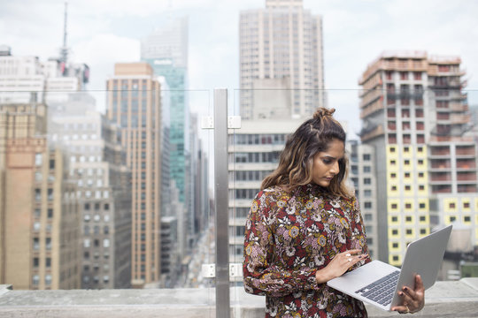 Woman looking at laptop while standing against glass window