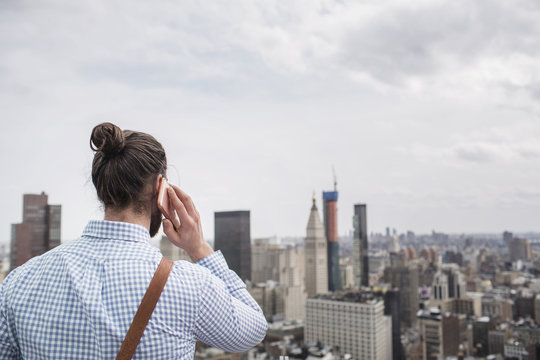 Rear view of man talking on phone while looking at cityscape