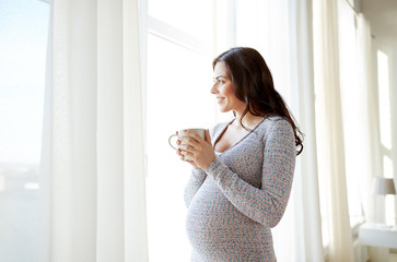 happy pregnant woman with cup drinking tea at home