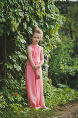 Portrait of a girl in a long dress among the shrubs of the garde