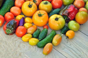Fototapeta na wymiar Crop of yellow and red tomatoes, cucumbers, sweet peppers on wooden surface. Food background.