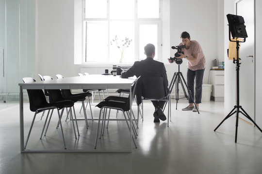 Man filming businessman sitting in boardroom