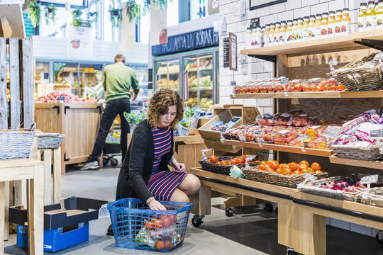 Young woman buying tomatoes while crouching in supermarket