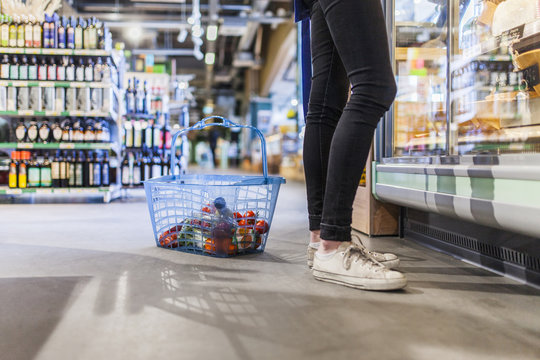 Low section of young man standing by shopping basket in supermarket