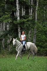 Beauty blond girl riding horse in woods 