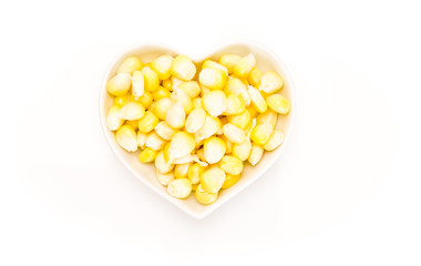 Corn kernels in a heart shaped white bowl, on white background.