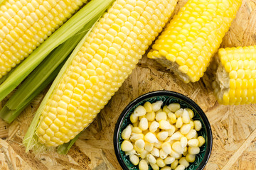 Corn cobs and a bowl of kernels, on wooden background.