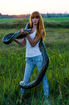 beautiful portrait of a red-haired girl with a snake at sunset   